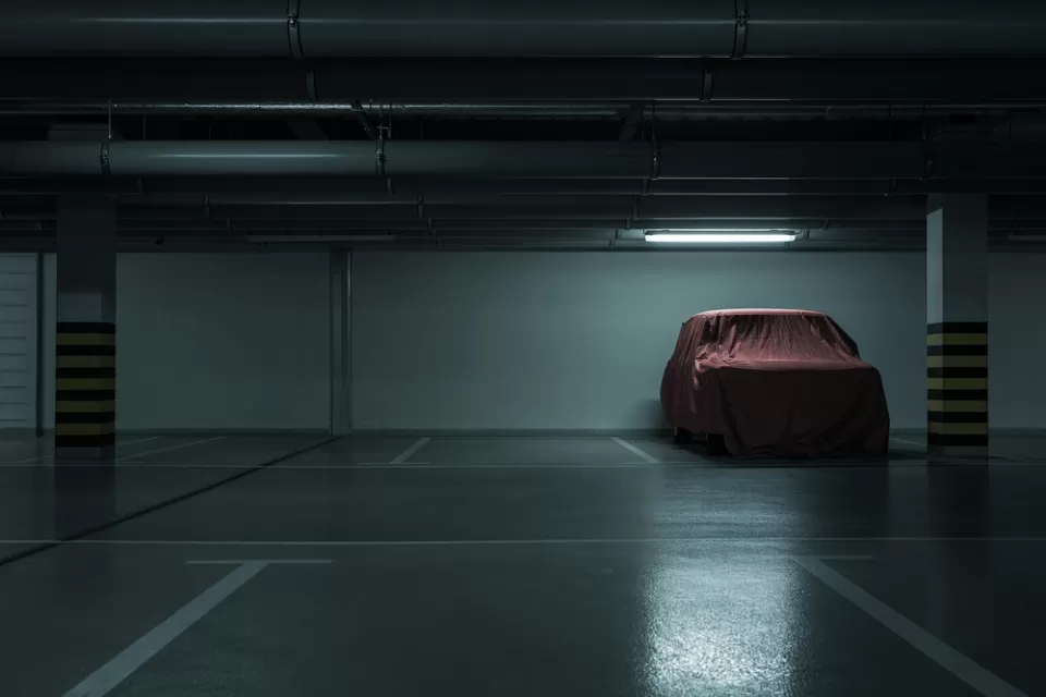 Dark parking garage, empty except for one car covered with a red tarp